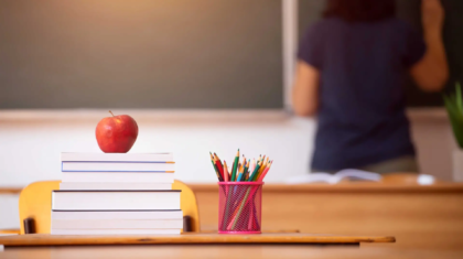 Pencils, apple and books, teacher and blackboard in the background.