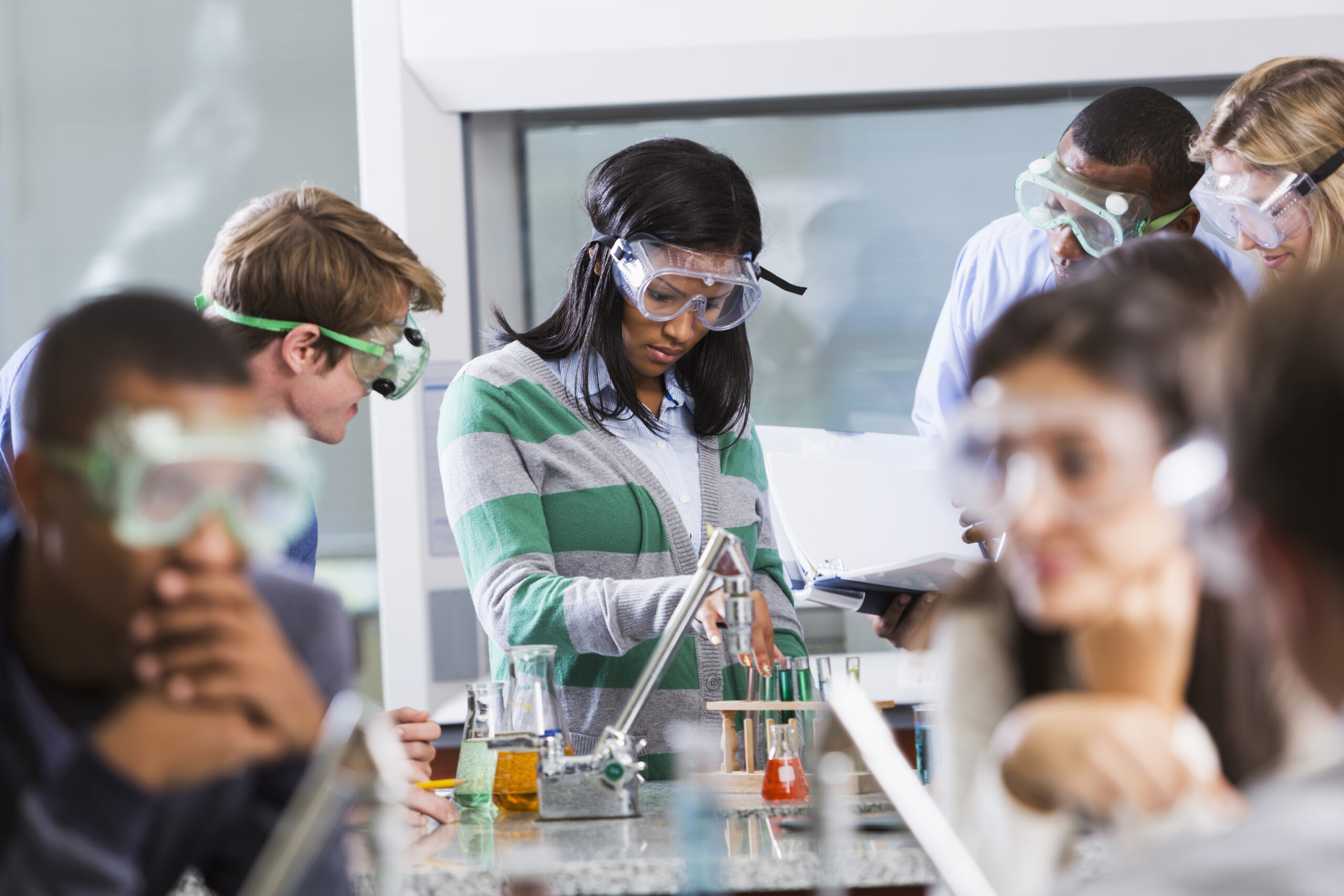 Students in a classroom completing a science experiment, with help from a teacher.