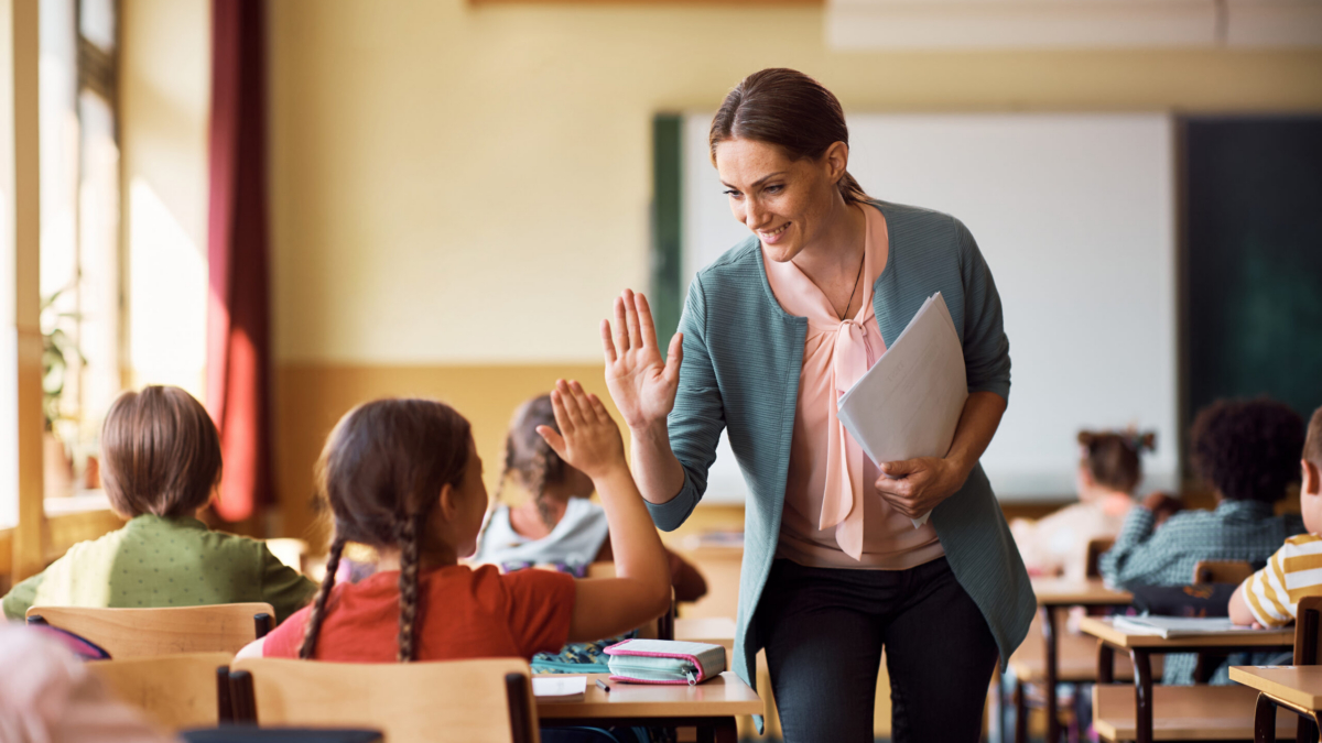 Happy teacher and schoolgirl giving high five during class at school.